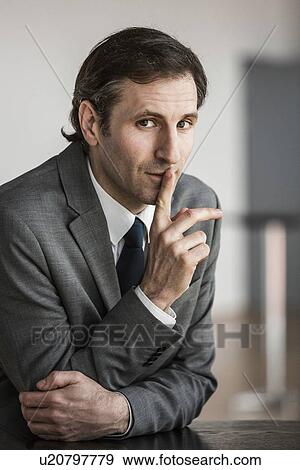 Stock Photo - Portrait of mature businessman, finger to lips. Fotosearch