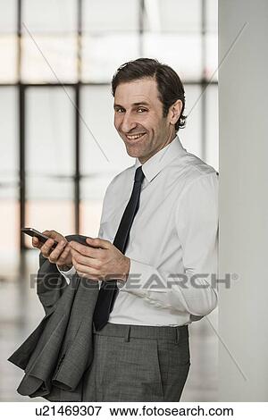 Stock Photo - Portrait of mature businessman, using smartphone, smiling. Fotosearch