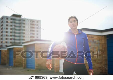 Stock Image - Portrait of mature female basketball player holding ball. Fotosearch