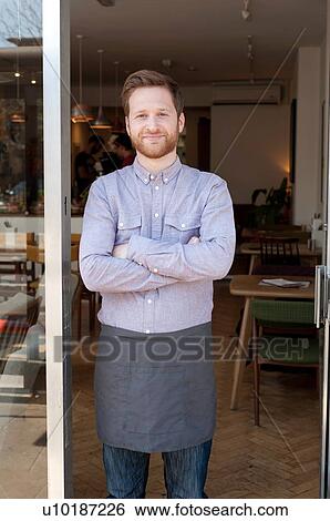 Stock Photograph - Portrait of proud young male cafe owner in doorway. Fotosearch