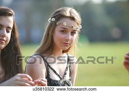Stock Image - Portrait of teenage girl wearing daisy chain headdress in park. Fotosearch