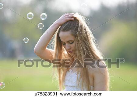 Stock Image - Portrait of teenage girl with hand in hair in park. Fotosearch