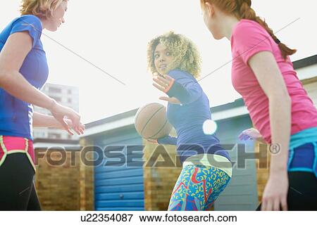 Stock Photo - Portrait of three women exercising together playing basketball. Fotosearch