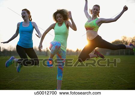 Stock Image - Portrait of three women jumping in the park. Fotosearch