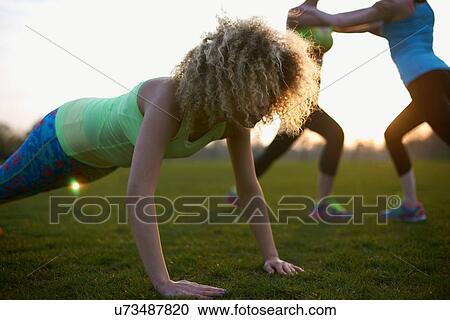 Stock Image - Portrait of woman doing push up exercise in park. Fotosearch