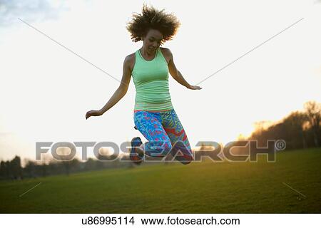Picture - Portrait of woman jumping in park. Fotosearch