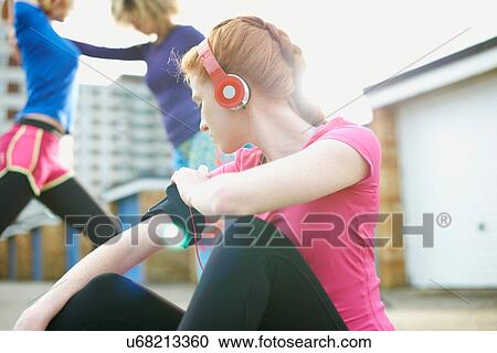 Stock Image - Portrait of woman sitting on floor attaching armband before exercise. Fotosearch