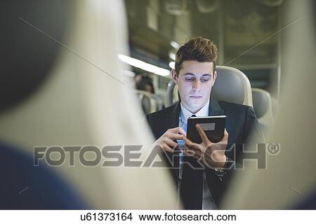 Picture - Portrait of young businessman commuter using digital tablet on train.. Fotosearch