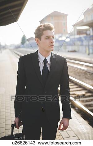 Stock Image - Portrait of young businessman commuter standing on railway platform.. Fotosearch