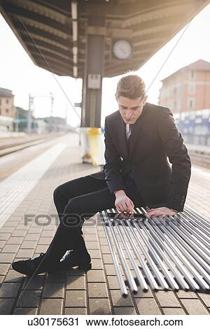 Stock Image - Portrait of young businessman commuter using digital tablet at train station.. Fotosearch