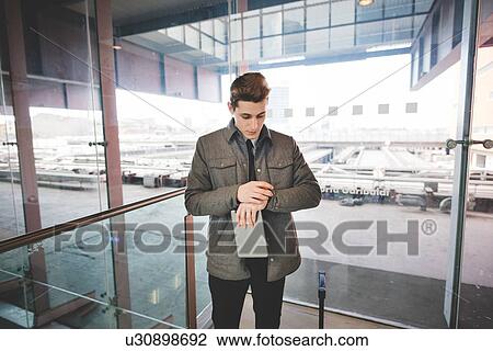 Stock Image - Portrait of young businessman commuter checking wristwatch for time.. Fotosearch