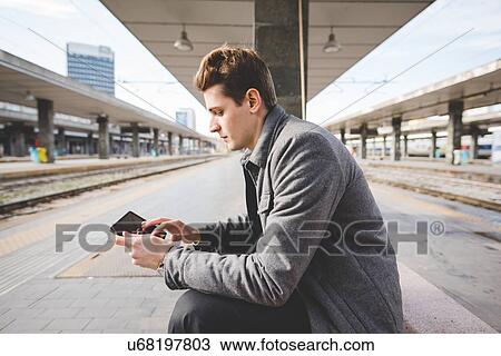 Stock Image - Portrait of young businessman commuter using digital tablet at train station.. Fotosearch