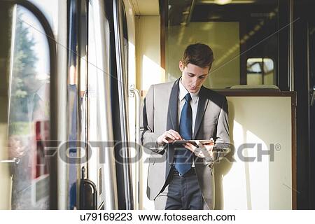 Stock Image - Portrait of young businessman commuter using digital tablet on train.. Fotosearch