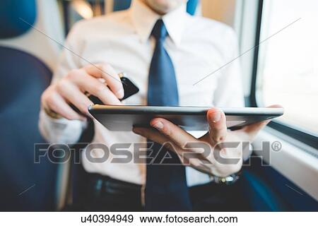Stock Photo - Portrait of young businessman commuter using digital tablet on train.. Fotosearch