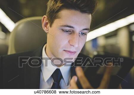 Stock Photo - Portrait of young businessman commuter using digital tablet on train.. Fotosearch