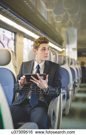 Stock Photograph - Portrait of young businessman commuter using digital tablet on train.. Fotosearch