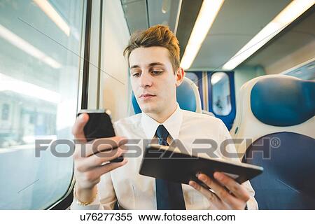 Stock Photography - Portrait of young businessman commuter using digital tablet on train.. Fotosearch