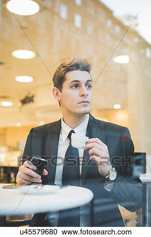 Stock Image - Portrait of young businessman sitting in cafe using digital tablet and mobile phone.. Fotosearch