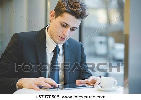 Portrait of young businessman sitting in cafe using digital tablet and mobile phone. View Large Photo Image Stock Photo - Portrait of young businessman sitting in cafe using digital tablet and mobile phone.. Fotosearch