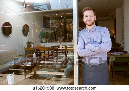 Stock Photo - Portrait of young male cafe owner with arms folded in doorway. Fotosearch