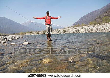 Stock Image - Portrait of young male hiker standing on Toce river rock, Vogogna, Verbania, Piemonte, Italy. Fotosearch