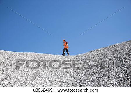 Stock Image - Quarry worker chatting on smartphone on top of quarry gravel mound. Fotosearch