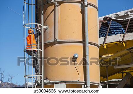 Stock Photograph - Quarry worker climbling smoke stack ladder at gravel quarry. Fotosearch