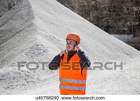 Stock Image - Quarry worker fastening helmet at gravel quarry. Fotosearch