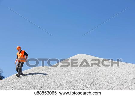 Stock Photography - Quarry worker lmoving down steep gravel mound at quarry. Fotosearch