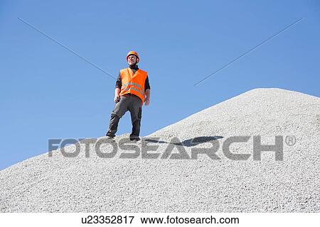 Stock Photo - Quarry worker looking out from gravel mound at quarry. Fotosearch