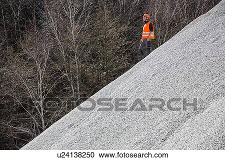 Stock Image - Quarry worker moving down gravel mound at quarry. Fotosearch