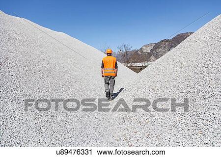 Stock Image - Quarry worker walking through gravel mounds at quarry. Fotosearch