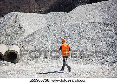 Stock Photograph - Quarry worker walking through gravel mounds at quarry. Fotosearch