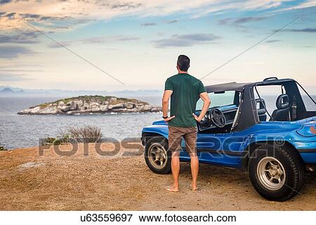 Stock Photo - Rear view of male tourist looking out to Branca island, Buzios, Rio de Janeiro, Brazil. Fotosearch