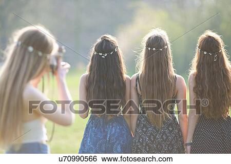 Rear view of teenage girl photographing friends wearing daisy chain headdresses in park View Large Photo Image Stock Photograph - Rear view of teenage girl photographing friends wearing daisy chain headdresses in park. Fotosearch