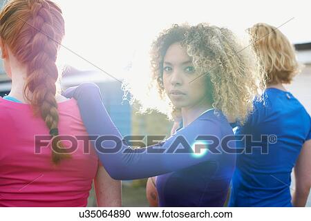 Stock Image - Rear view of three women exercising together with one woman looking at camera. Fotosearch