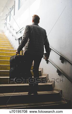 Stock Photo - Rear view of young businessman commuter on stairs carrying suitcase.. Fotosearch