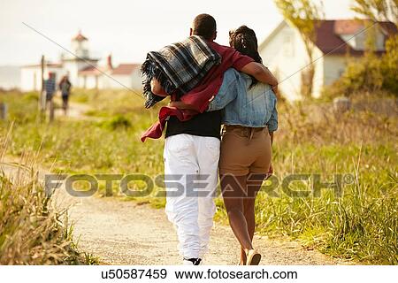 Rear view of young couple strolling with arms around each other View Large Photo Image Stock Photo - Rear view of young couple strolling with arms around each other. Fotosearch