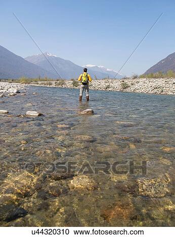 Stock Image - Rear view of young male hiker crossing Toce river, Vogogna, Verbania, Piemonte, Italy. Fotosearch