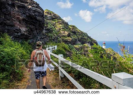 Stock Photo - Rear view of young male tourist walking towards Makapuu lighthouse, Oahu, Hawaii, USA. Fotosearch