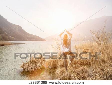Rear view of young woman practicing yoga on lakeside, Lake Mergozzo, Verbania, Piemonte, Italy View Large Photo Image Stock Photography - Rear view of young woman practicing yoga on lakeside, Lake Mergozzo, Verbania, Piemonte, Italy. Fotosearch