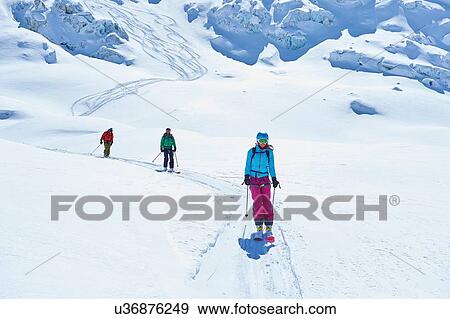 Stock Photo - Row of three adult skiers skiing down Mont Blanc massif, Graian Alps, France. Fotosearch