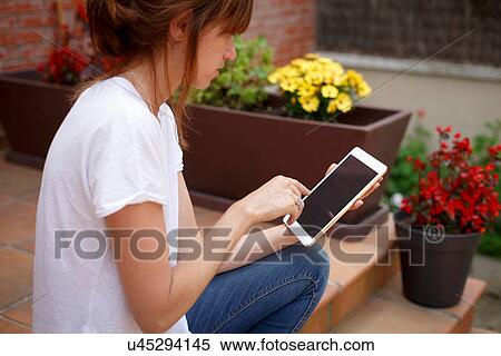 Stock Photography - Side view of mid adult woman sitting outdoors using digital tablet. Fotosearch