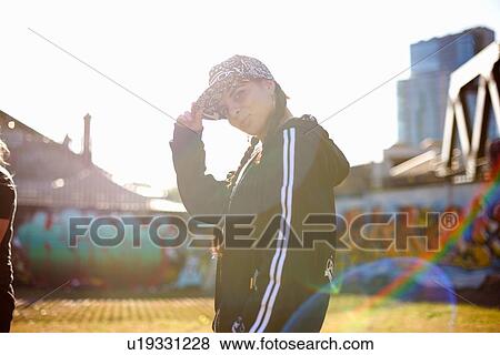 Stock Photo - Side view of young woman wearing baseball cap, looking at camera. Fotosearch