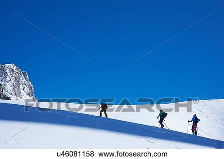 Stock Photo - Silhouetted view of three skiers moving up Mont Blanc massif, Graian Alps, France. Fotosearch