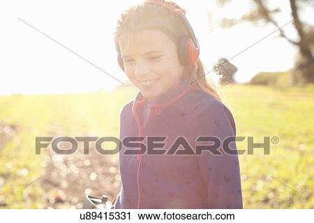 Stock Image - Smiling girl wearing headphones metal detecting in field. Fotosearch
