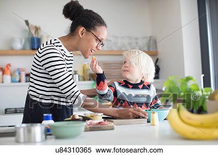 Son feeding mother food in kitchen View Large Photo Image Stock Photography - Son feeding mother food in kitchen. Fotosearch