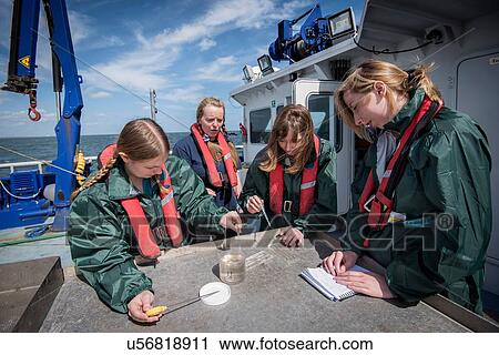 Stock Image - Student marine biologists test sea water sample on research ship. Fotosearch