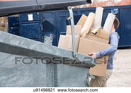 Stock Image - Teenage boy carrying cardboard waste to recycling bin. Fotosearch