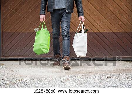 Stock Image - Teenage boy carrying reusable shopping bags full of empty bottles for recycling. Fotosearch